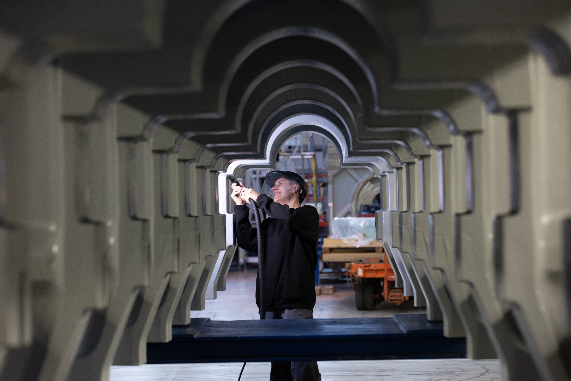 Worker welding large-scale industrial components inside a modern manufacturing facility.