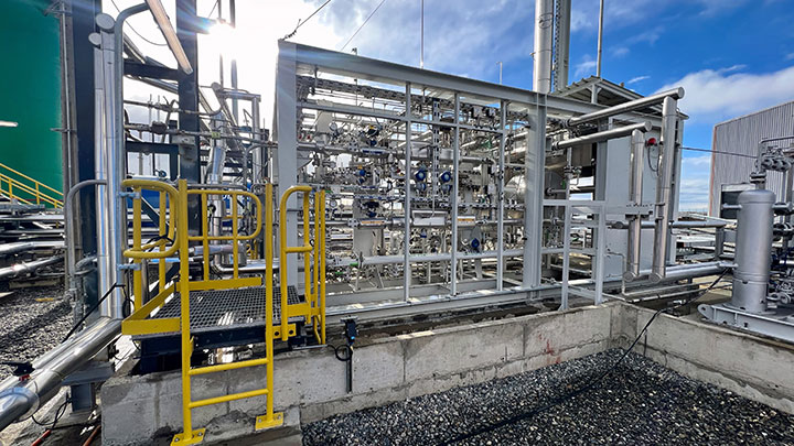 Green methanol reactor surrounded by pipes and industrial equipment on a bright, sunny day