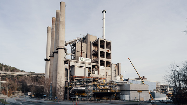 Large Heidelberg Materials cement plant with chimneys and exterior pipework on an overcast day