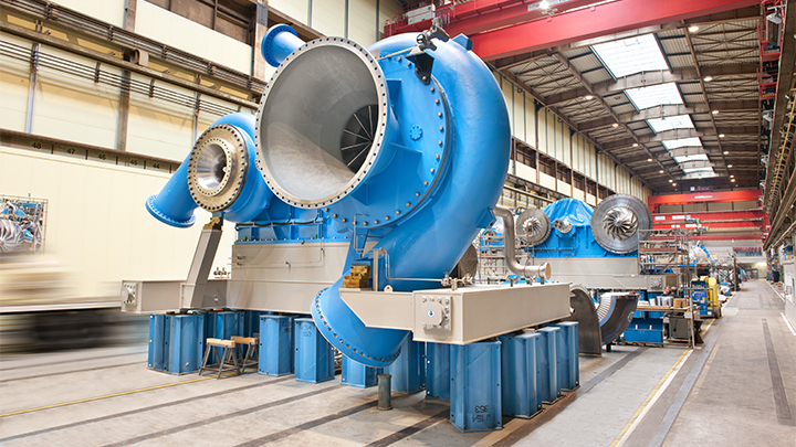 Large light blue industrial pump in a spacious, well-lit factory hall with surrounding machinery