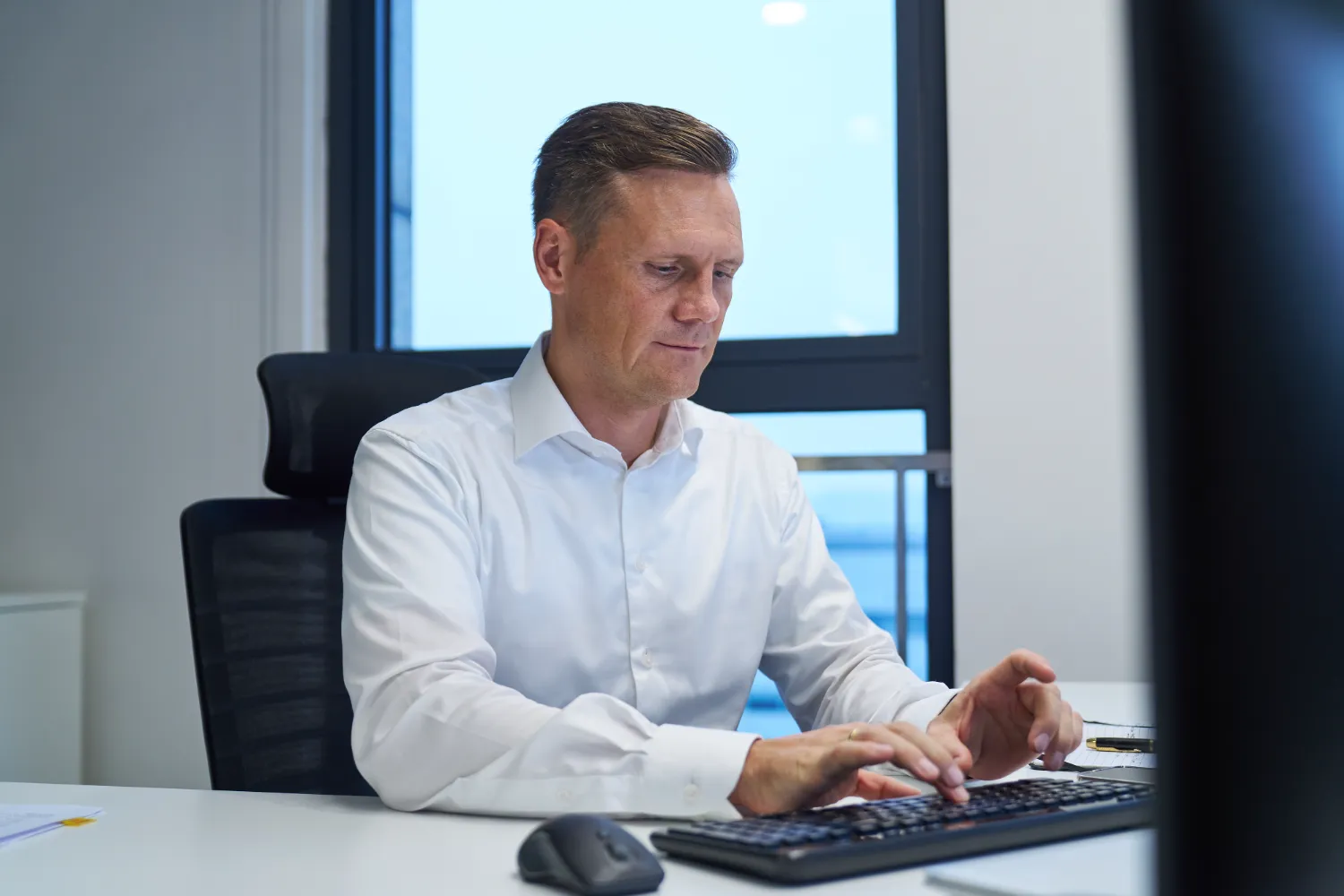 Person in a white shirt working at a desk with a computer, representing office-based coordination and planning for the Maersk Halifax retrofit.