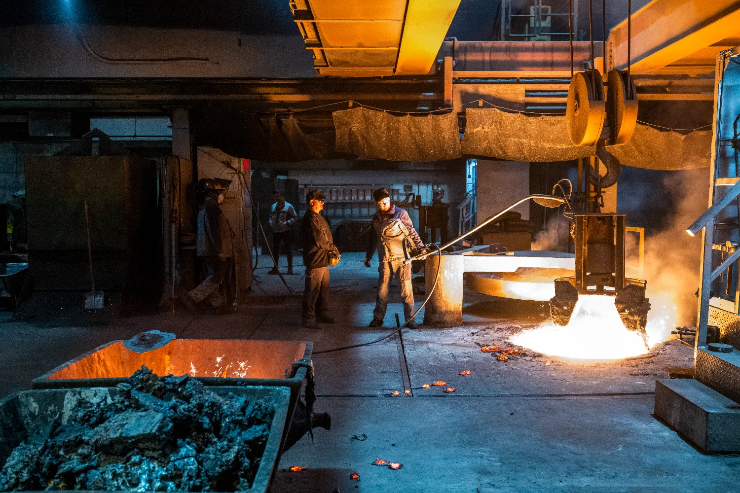Workers in protective gear handle molten iron using casting machinery inside the Everllence foundry in Augsburg