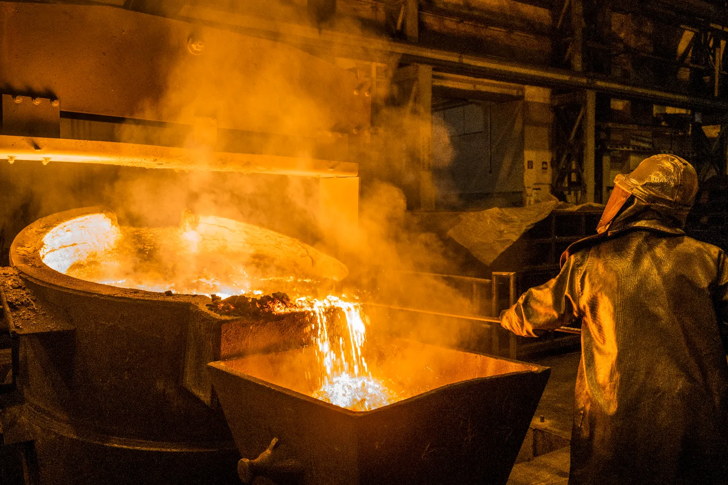 A worker pours glowing molten iron into a sand mold, with steam rising from the casting process.