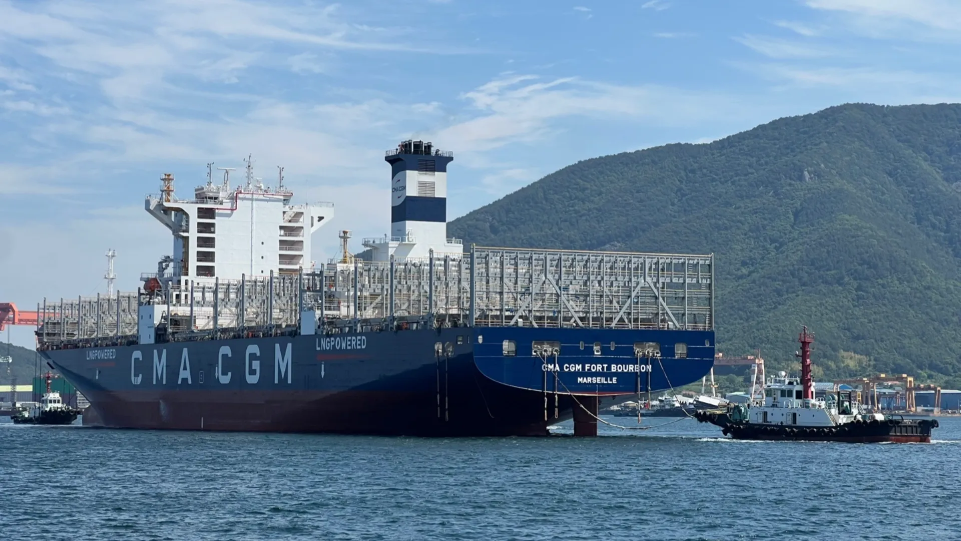The CMA CGM Fort Bourbon sails across open waters with mountains in the background, showcasing LNG-powered shipping in action