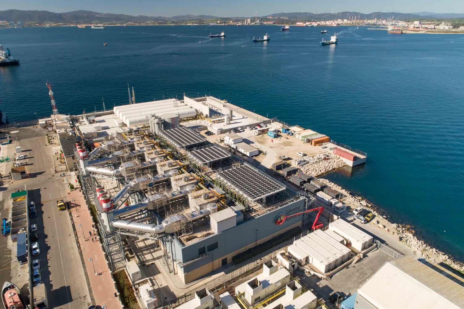 Aerial shot of a coastal power plant facility with multiple buildings and infrastructure near the shoreline, representing decentralized energy generation.