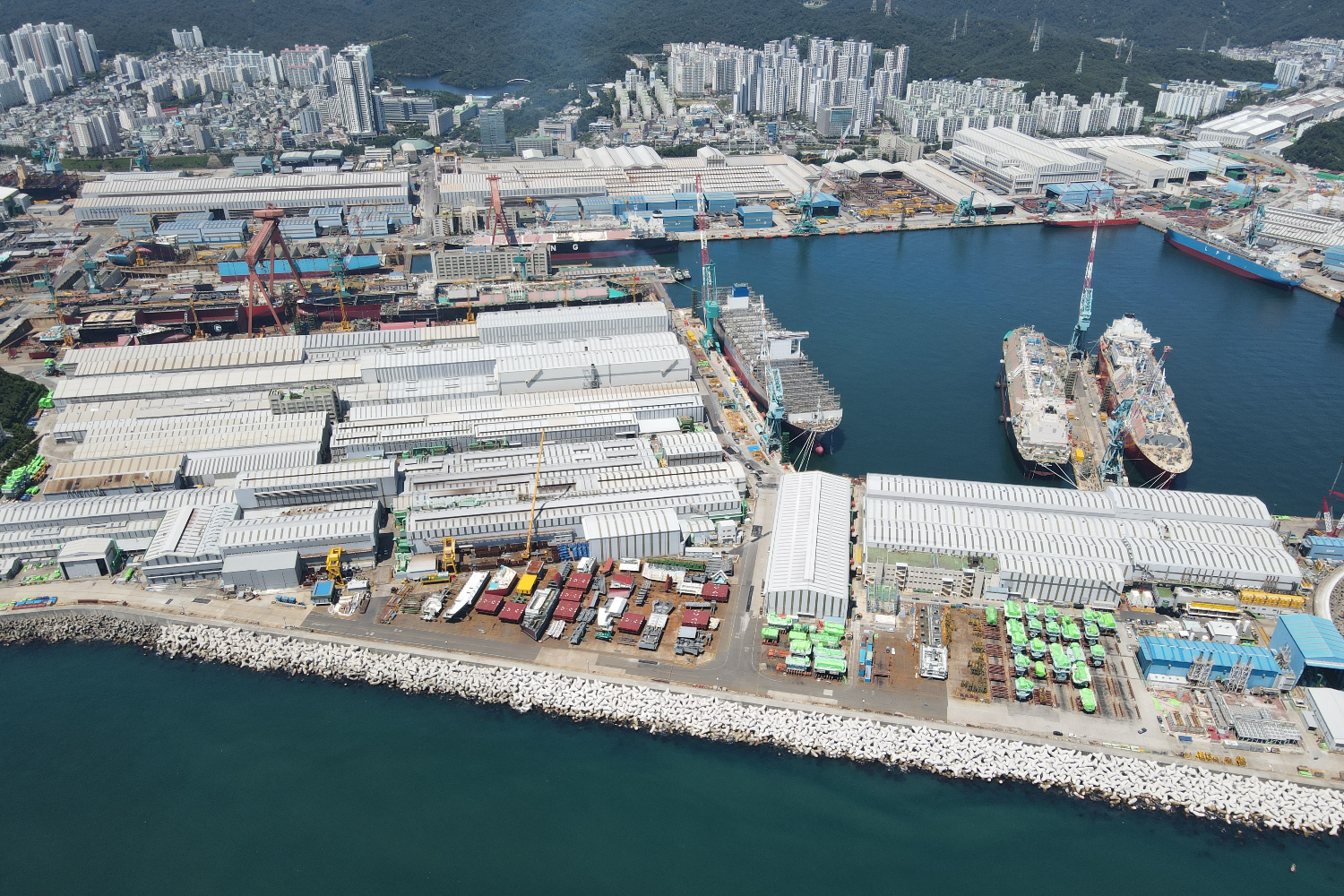 Aerial view of a large shipyard with docks, industrial buildings, and multiple vessels under construction along the coastline
