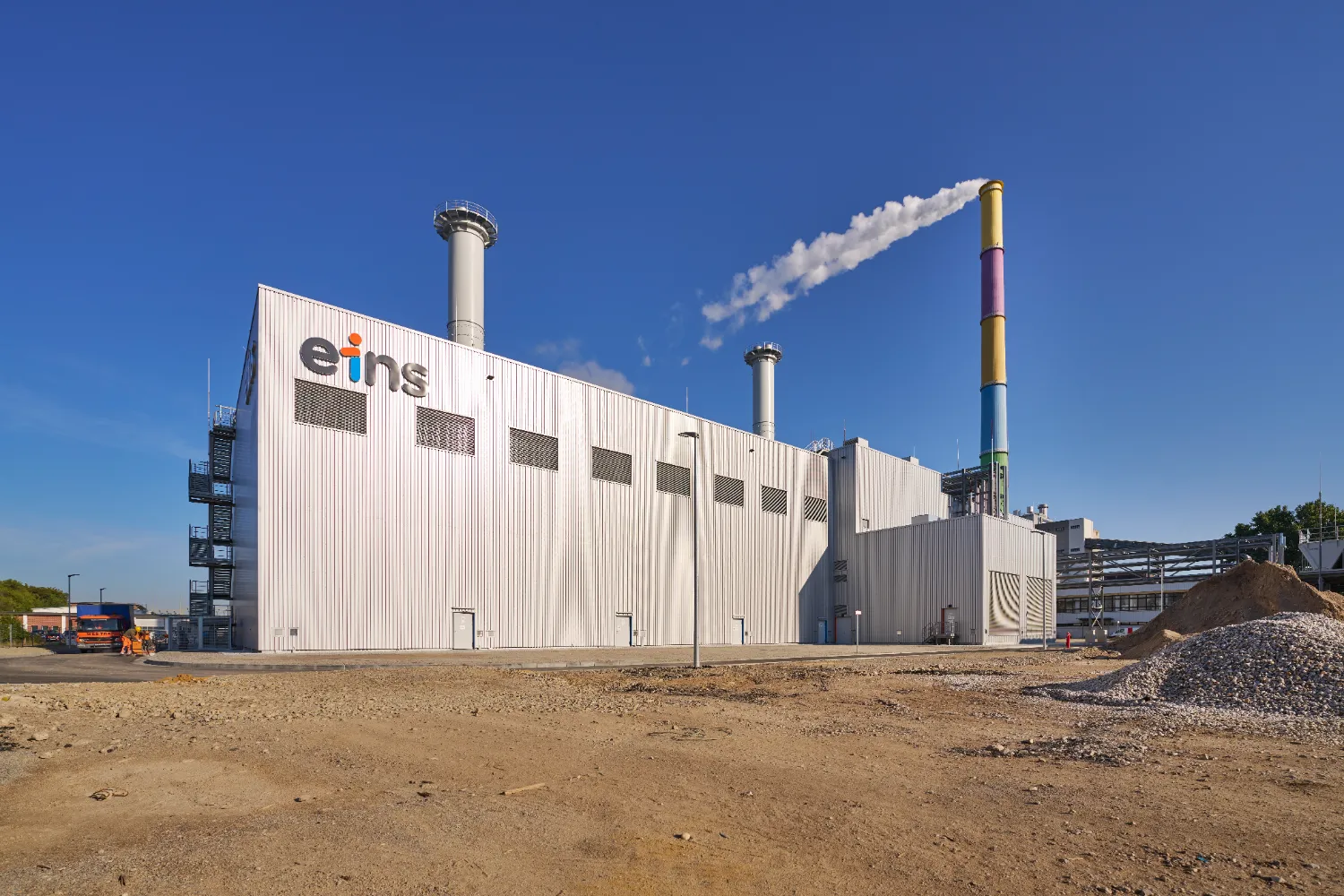 A large industrial building labeled “eins” with a tall chimney emitting smoke, representing the old coal-fired power plant in Chemnitz, Germany.
