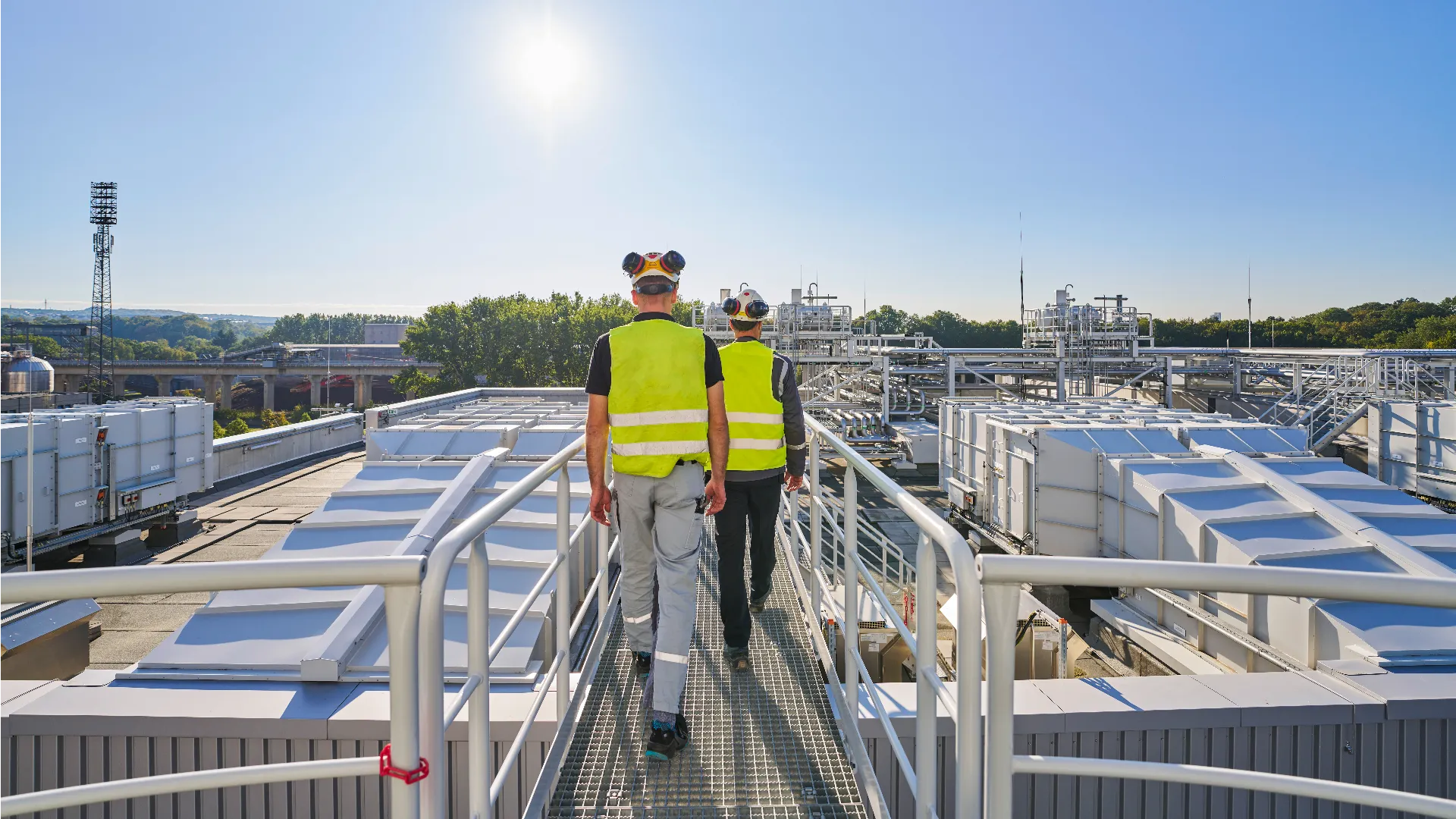 Two engineers in safety gear standing on a rooftop platform overlooking HVAC units at the MHKW Chemnitz-Nord CHP plant in Chemnitz, Germany.