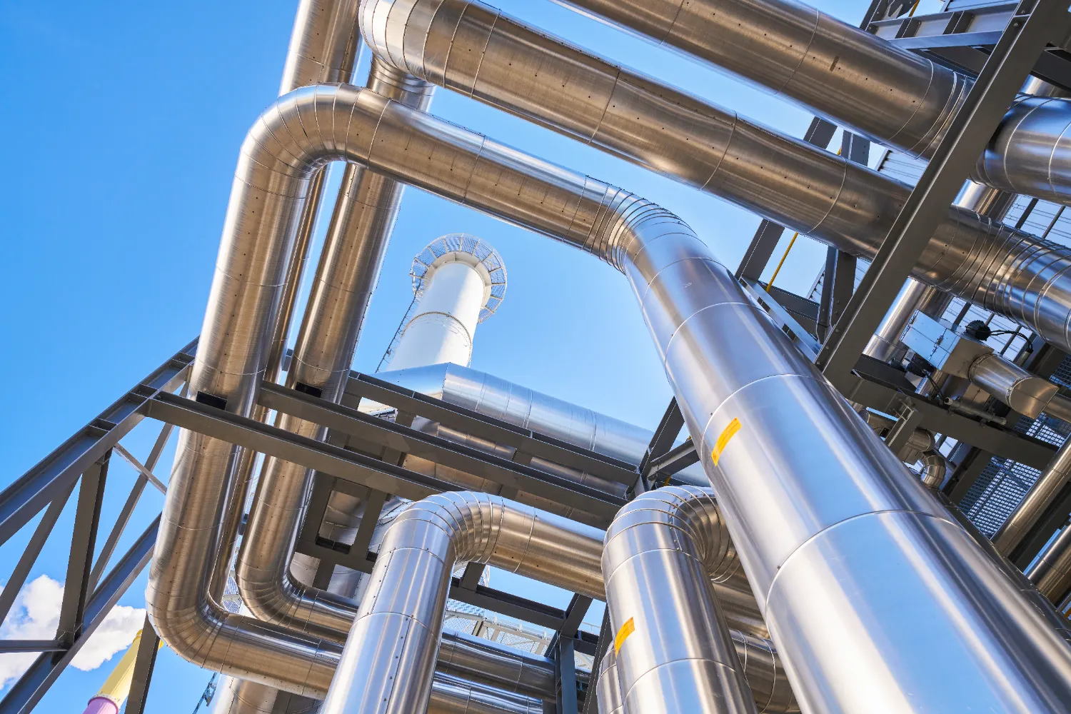 Shiny metal exhaust pipes extending upward against a clear blue sky, part of the heat recovery system at the Chemnitz-Nord gas engine power plant.