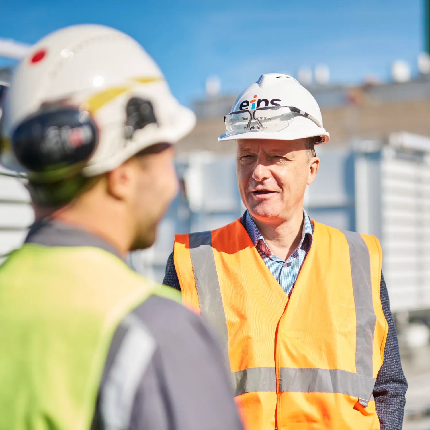 Tino Schlemmer in Safety gear. Project Manager at eins energie in sachsen. Back of another engineer in safety gear.