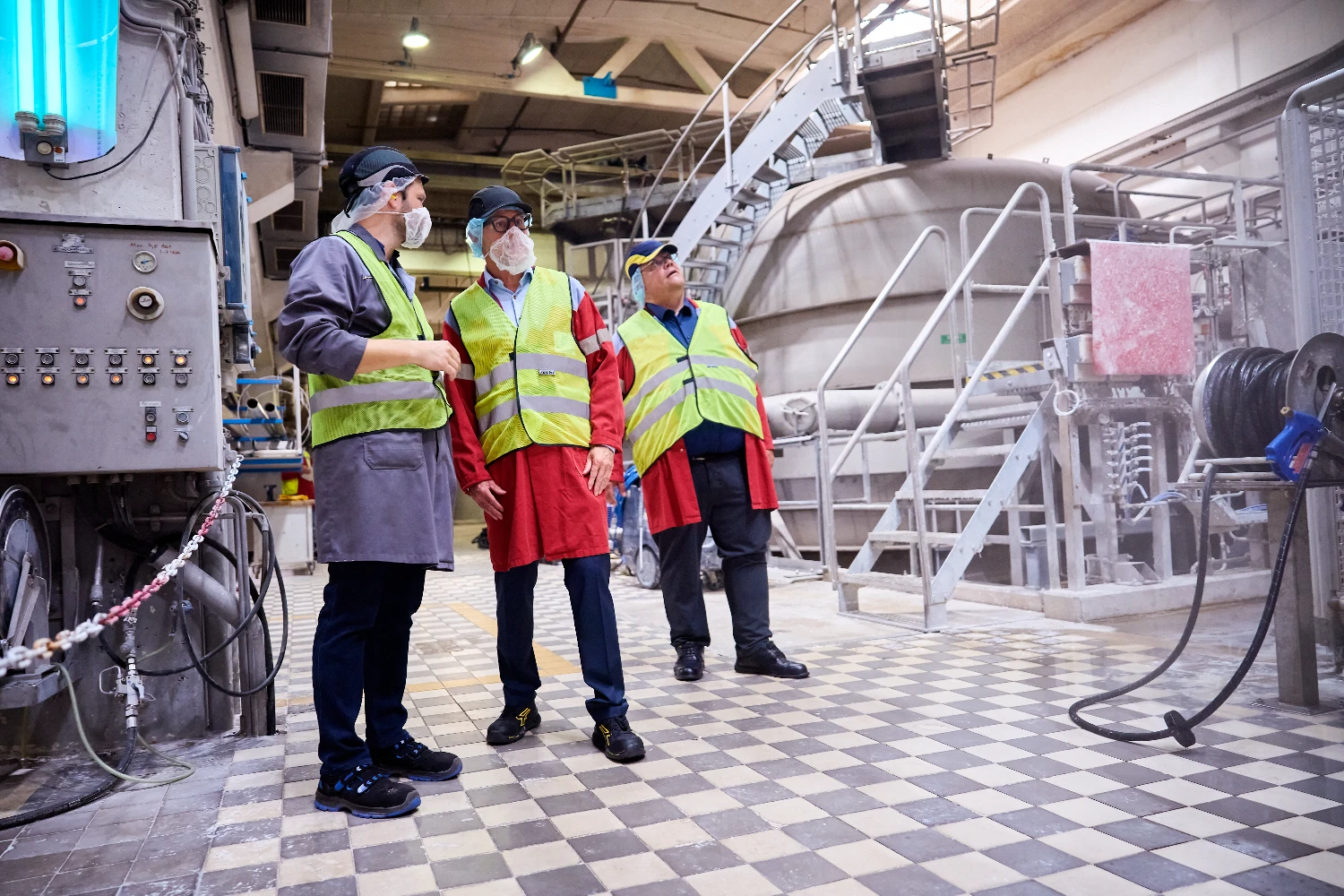 Workers in safety gear standing beside machinery on the factory floor.
