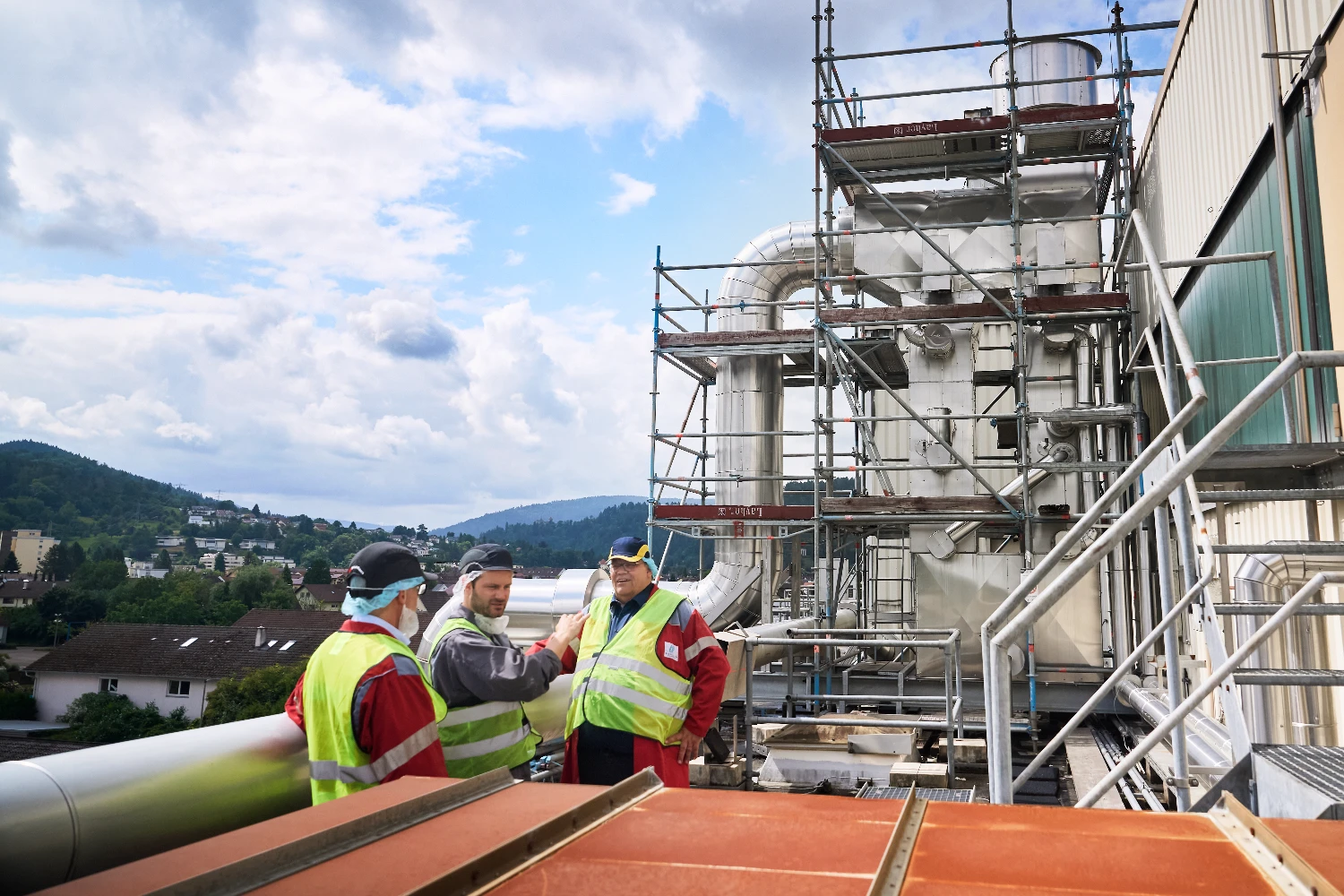 Workers standing on an exterior platform overlooking mill equipment.