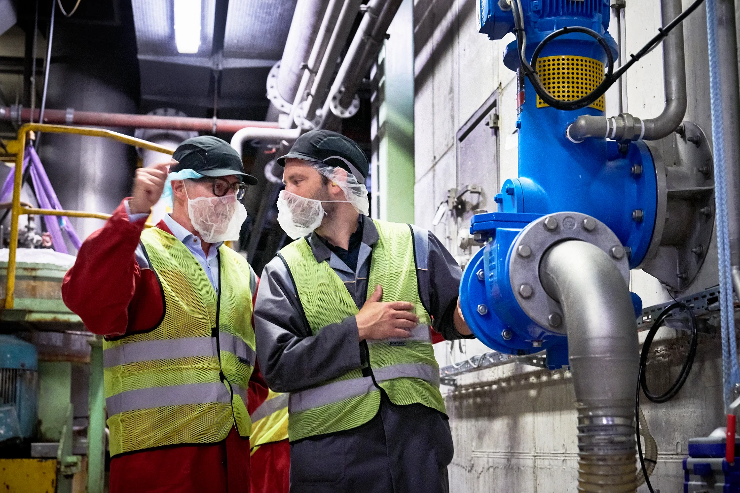 Two people in protective clothing examining large industrial pipes.