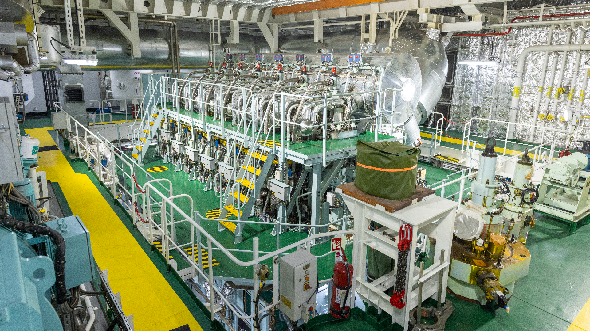 Wide shot of auxiliary engines inside a ship’s engine room, showing compact generator units connected to pipes and surrounded by maintenance walkways