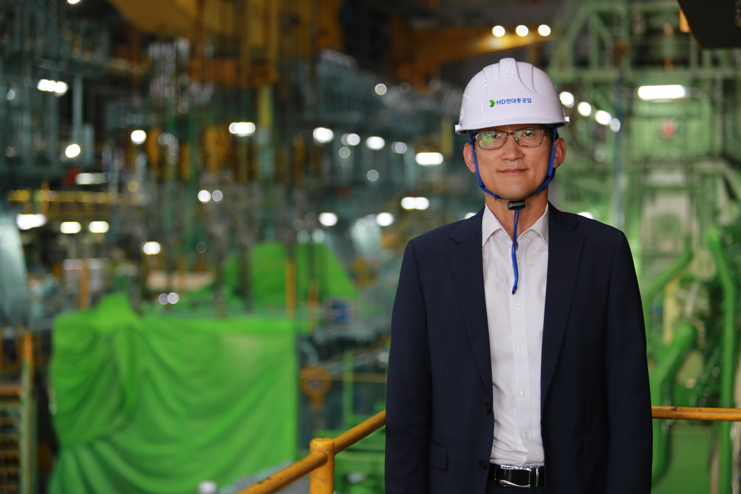 Person standing inside an industrial facility with green machinery and structural elements in the background