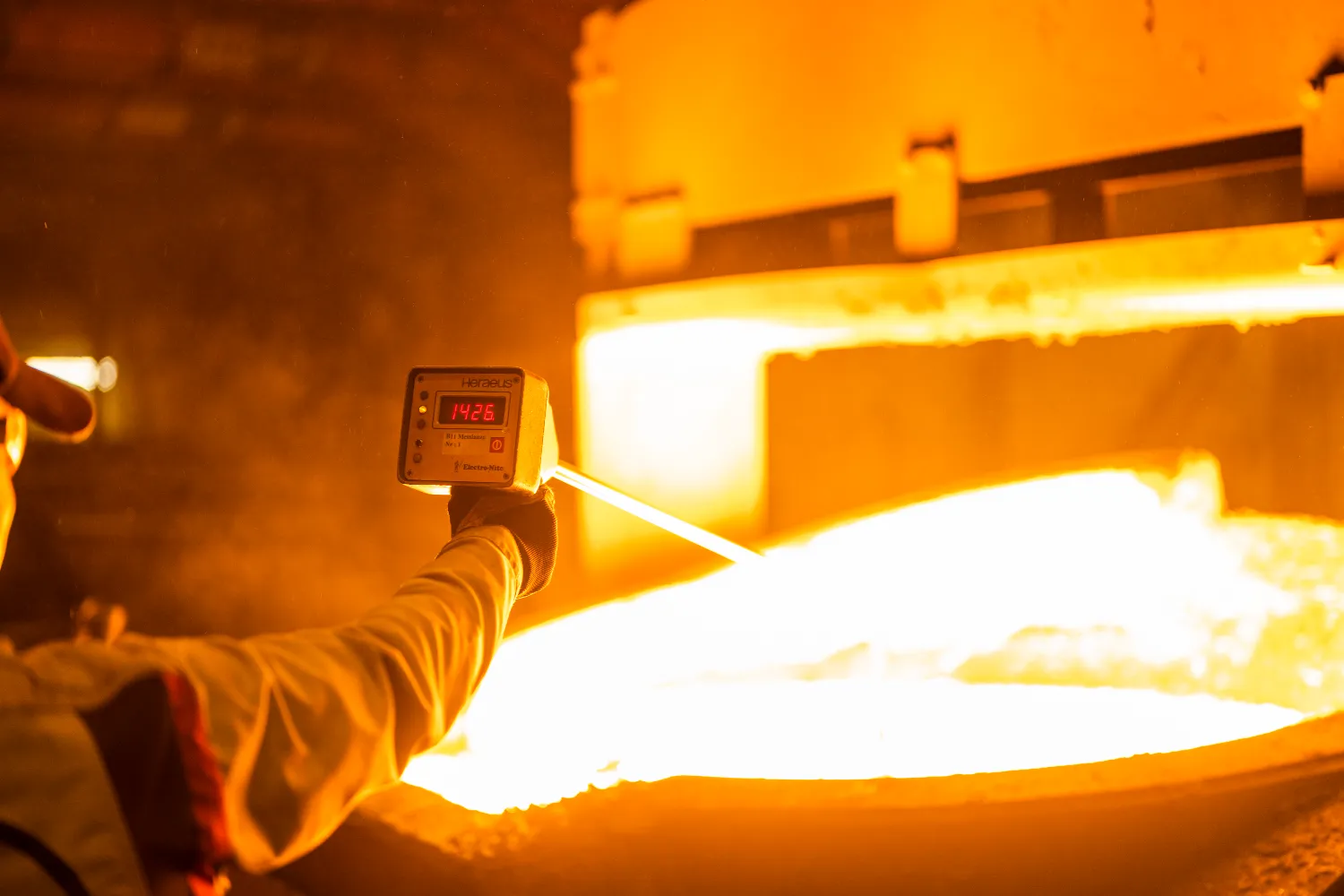 A worker uses an infrared thermometer to check the temperature of molten iron in a casting pot.