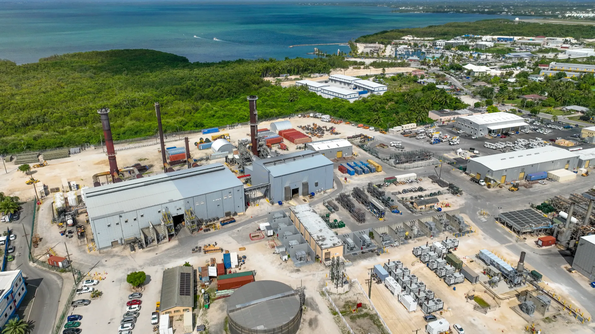 Aerial view of the Caribbean Utilities Company power plant on Grand Cayman, located near the coastline and surrounded by greenery.
