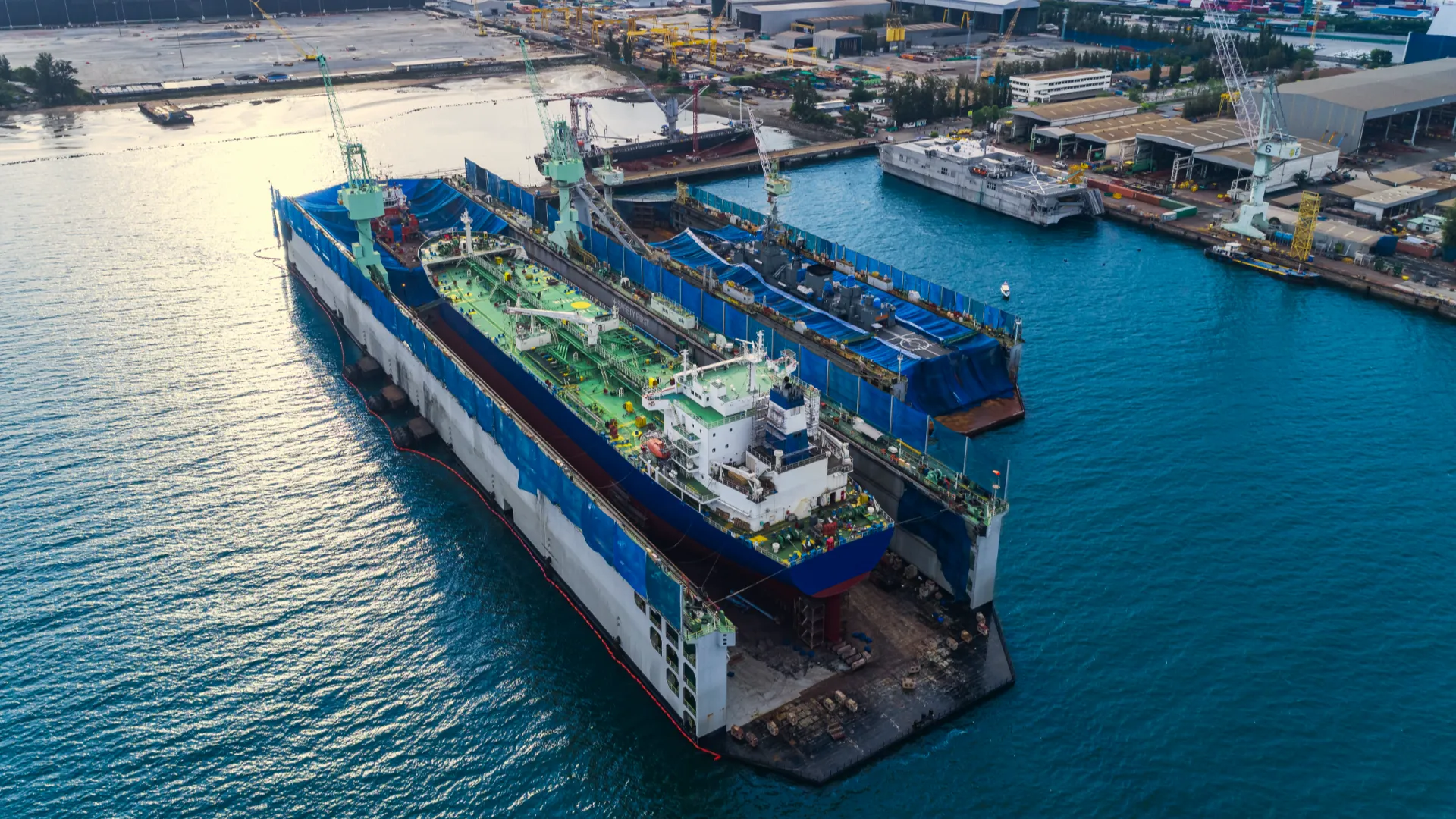 Aerial view of a shipyard showing two large vessels in dry docks surrounded by cranes and industrial equipment