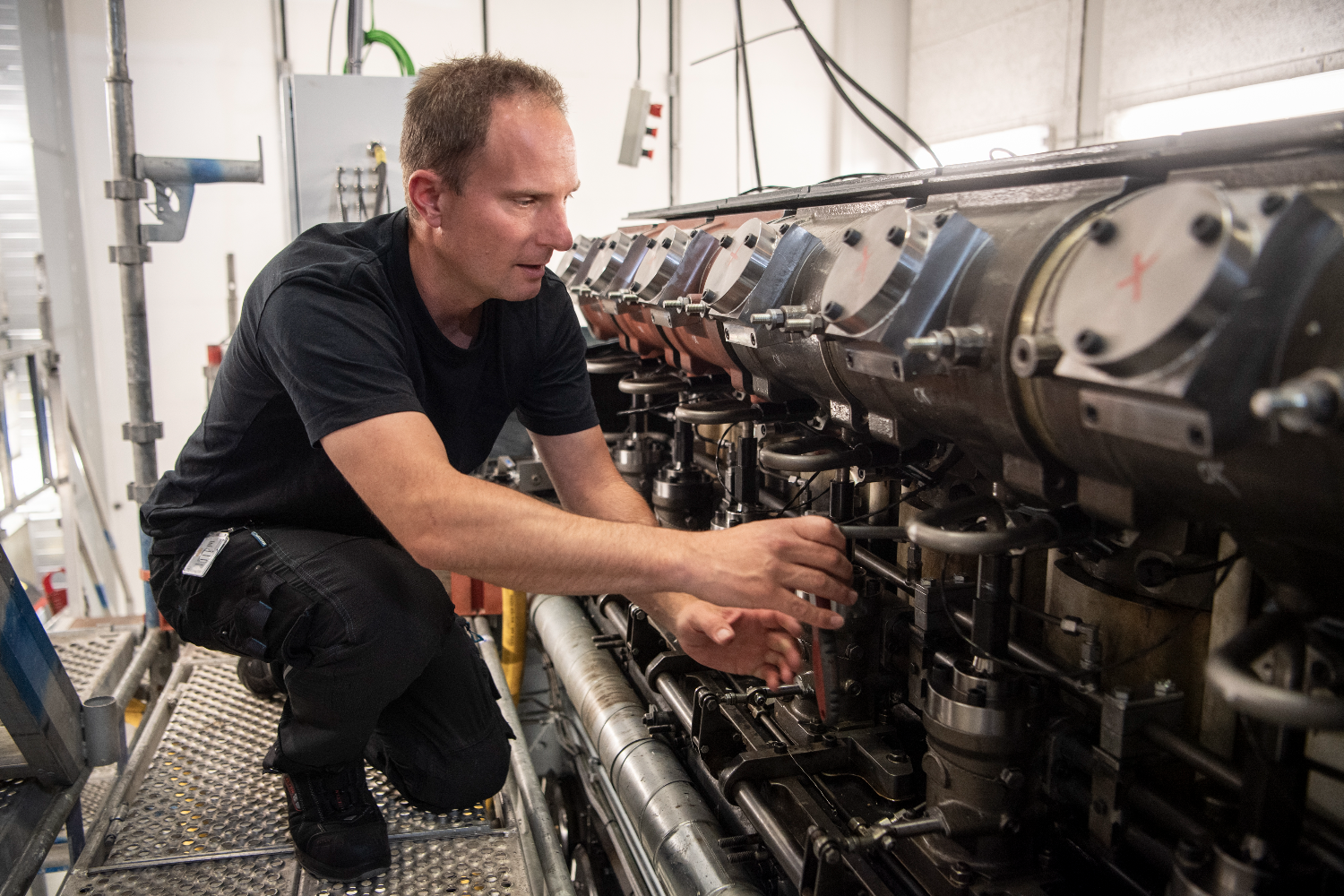 Engineer kneeling beside a row of engine cylinders, inspecting components along a large four-stroke methanol GenSet