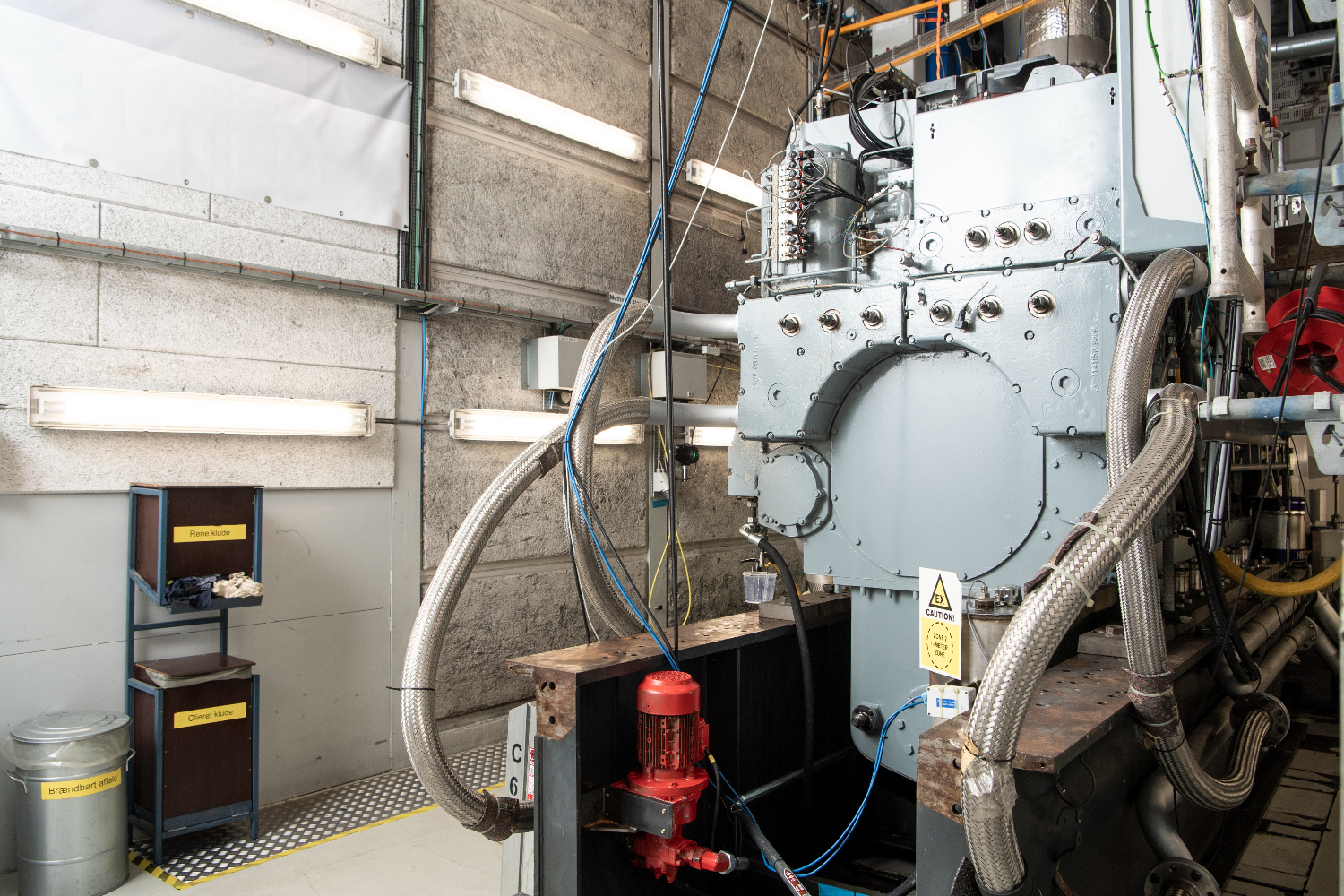 Wide view of a stationary dual-fuel methanol GenSet connected to exhaust ducts, piping, and auxiliary systems in a bright test hall