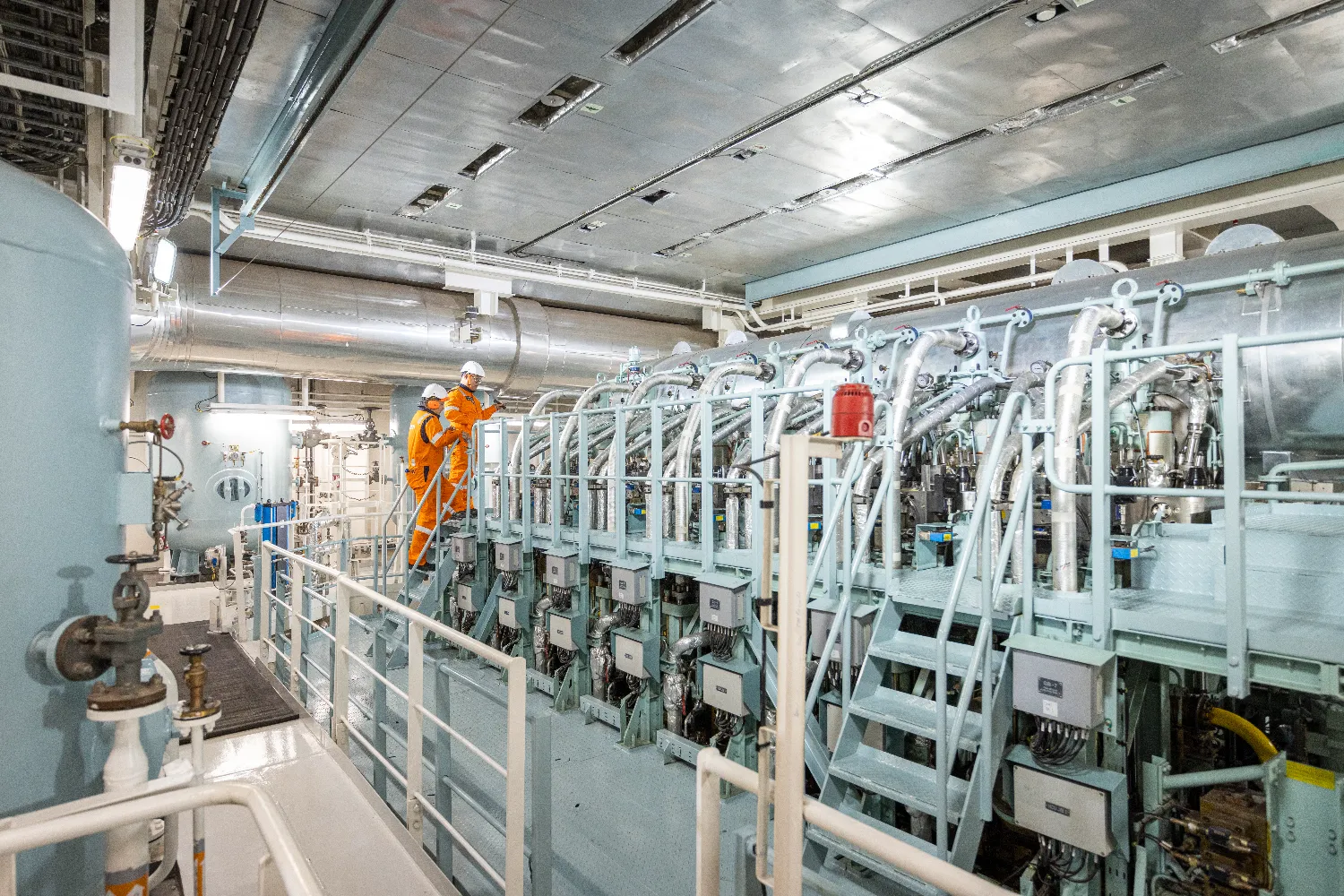 A crew member in orange overalls inspects the LNG-powered engine room aboard the Höegh Aurora, surrounded by complex machinery and piping systems