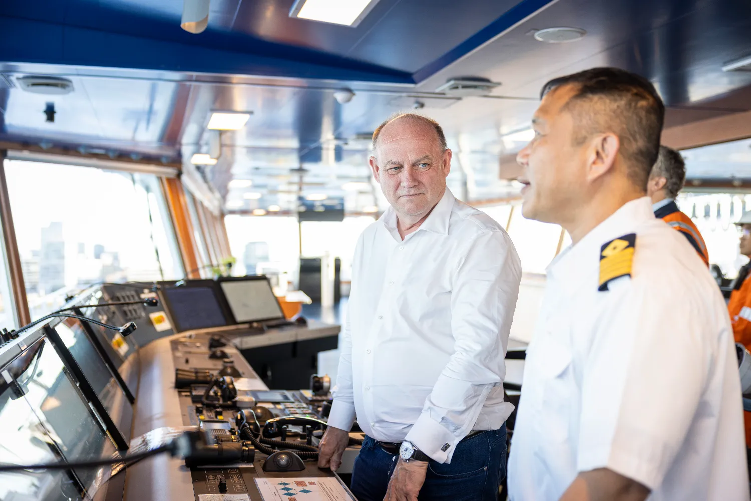 Two crew members interact on the bridge of the Höegh Aurora, surrounded by navigation systems and panoramic views of the sea during its maiden voyage.