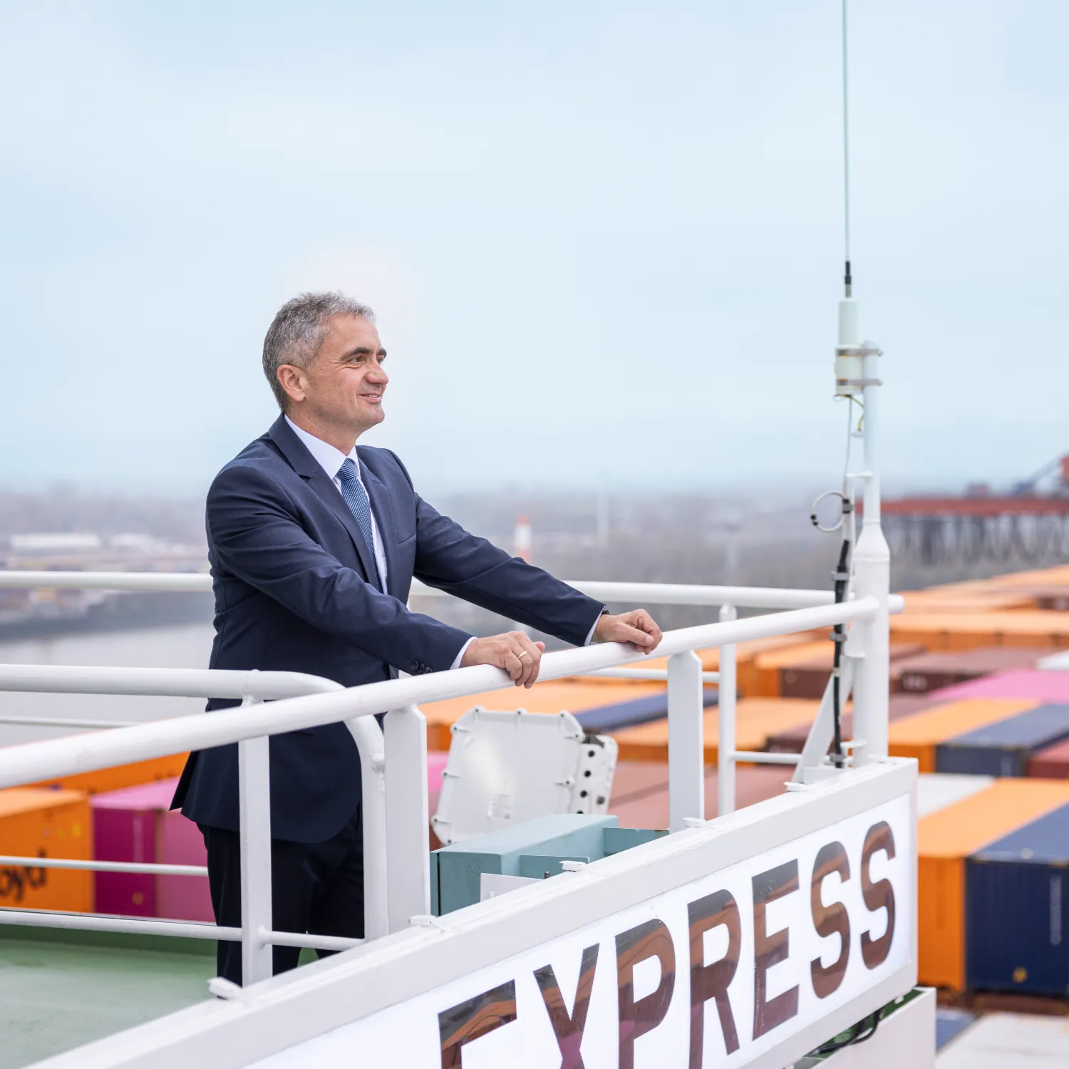Uwe Lauber standing on the deck of the Hamburg Express, with stacked containers and port cranes in the background during the ship’s naming ceremony.