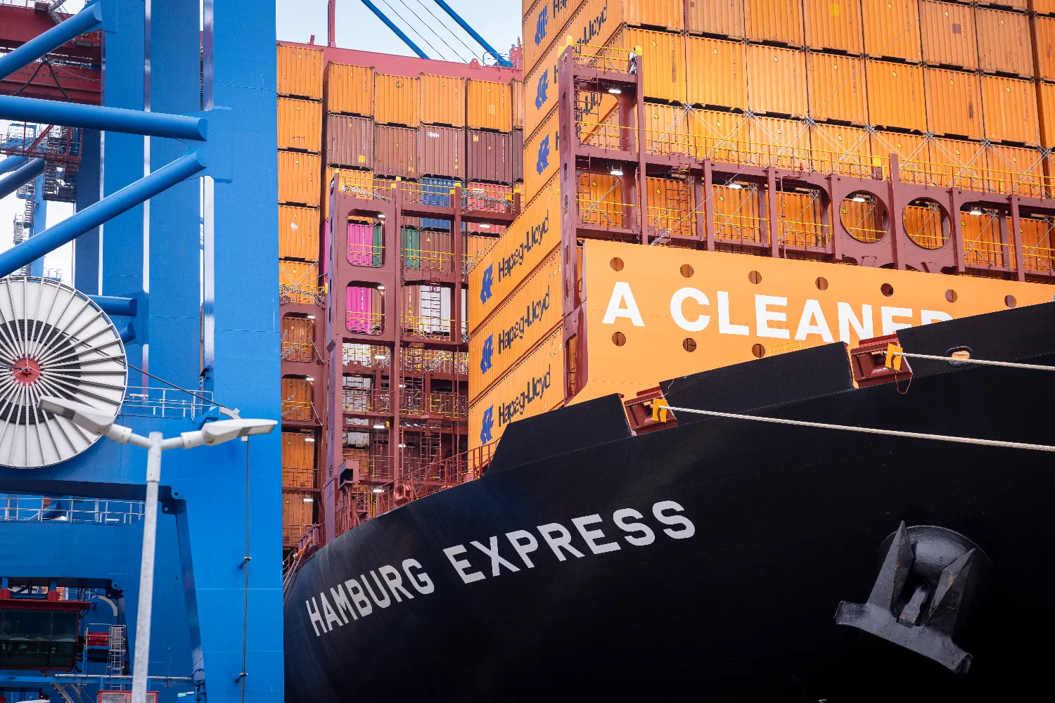 The Hamburg Express, a large Hapag-Lloyd container ship, docked at the Port of Hamburg with cranes and containers visible.