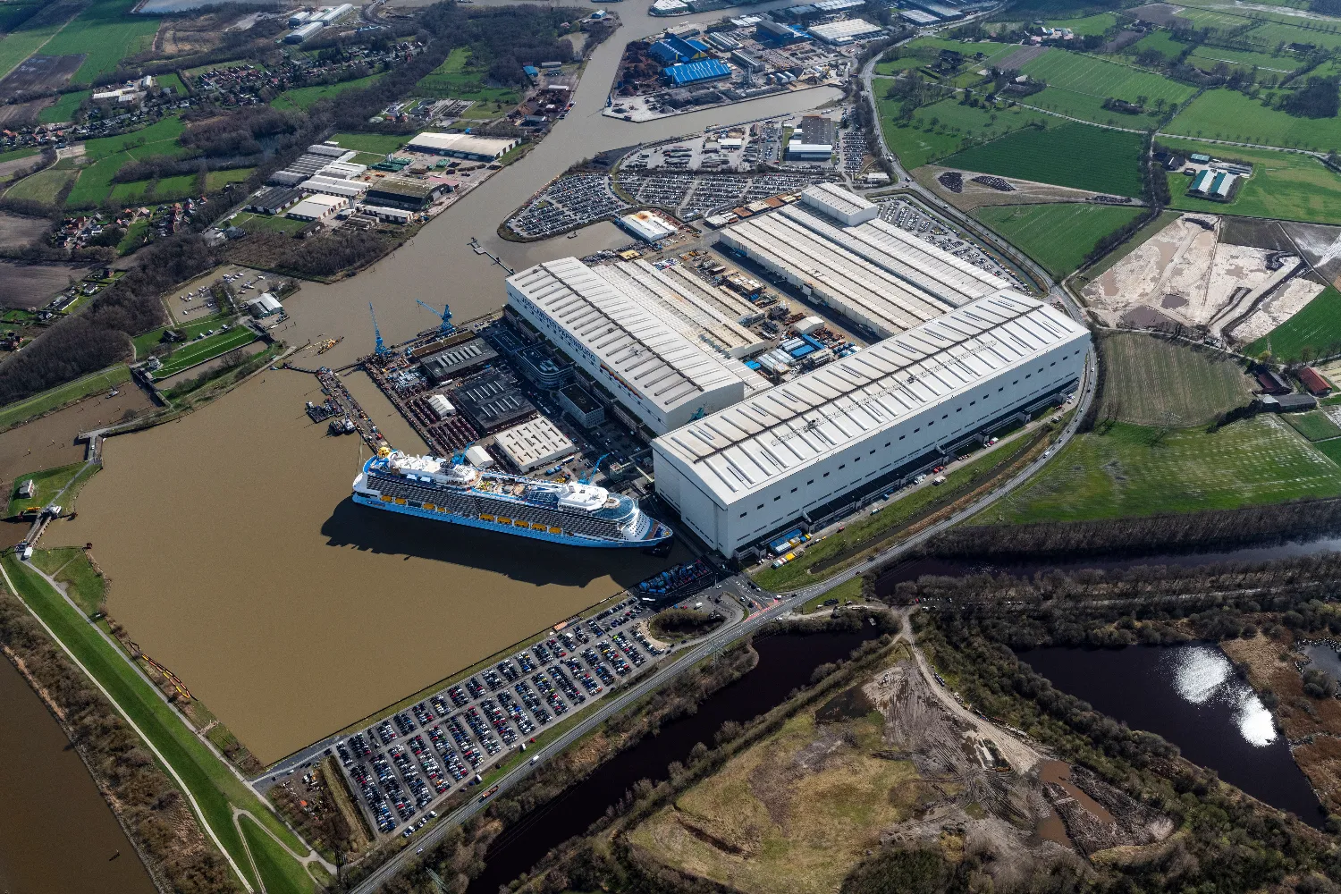 Aerial view of a large shipyard along a river with docks, cranes, buildings, and a cruise ship docked at MEYER WERFT in Papenburg, Germany