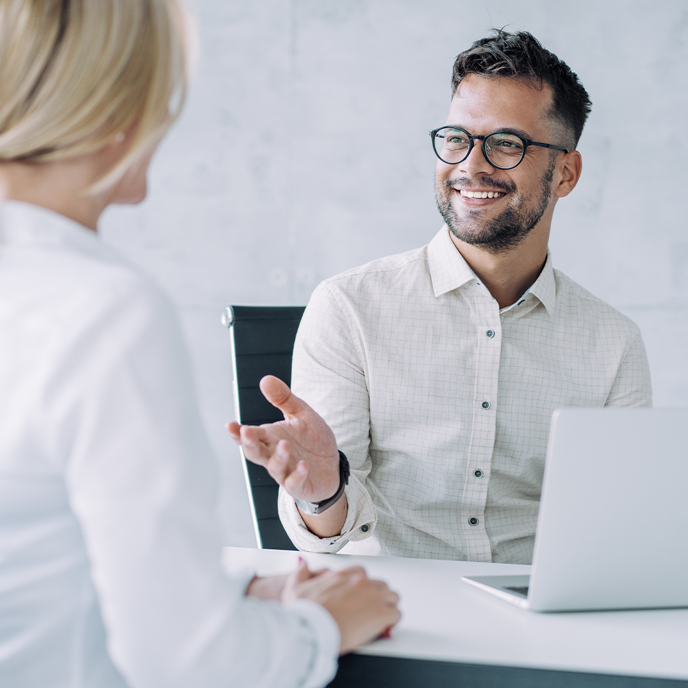 Smiling man talking with a woman at a desk in a bright office