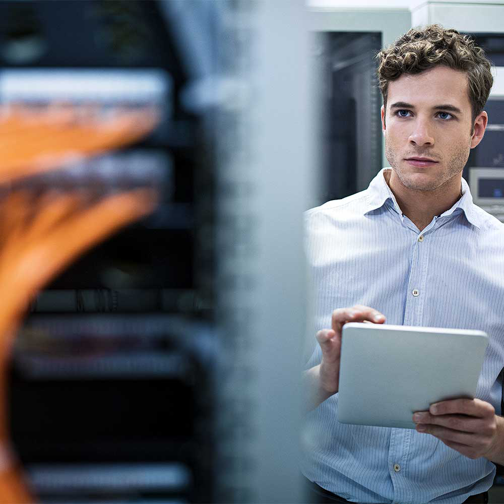 Man in server room holding tablet in front of network equipment