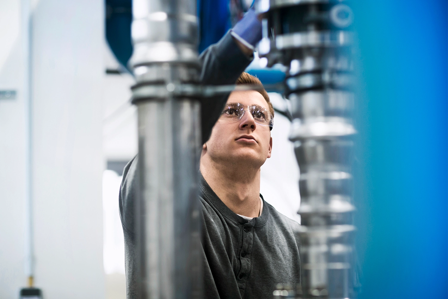 Man wearing safety glasses working with large metallic pipes indoors