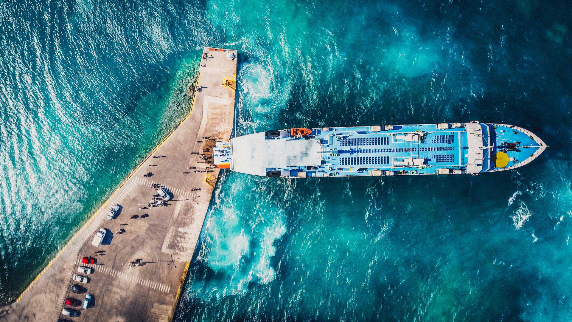 Aerial drone view of departing ferry at port with beautiful crystal blue water.