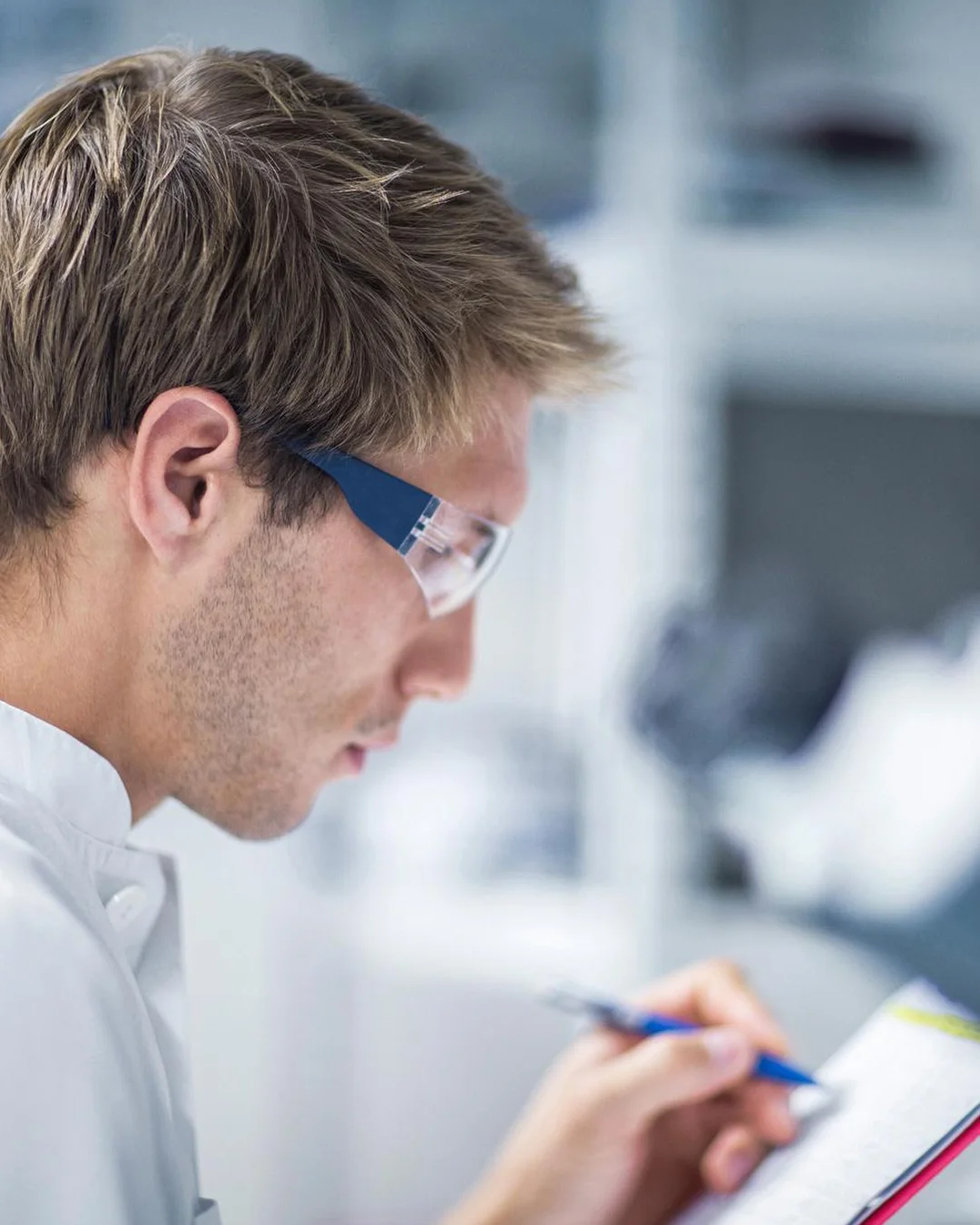 Man wearing safety glasses writing on a clipboard in a workshop