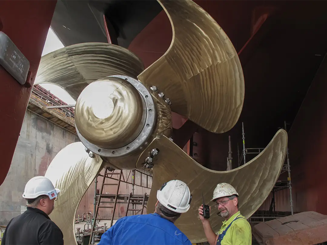 three people with helmets standing in front of a giant propeller