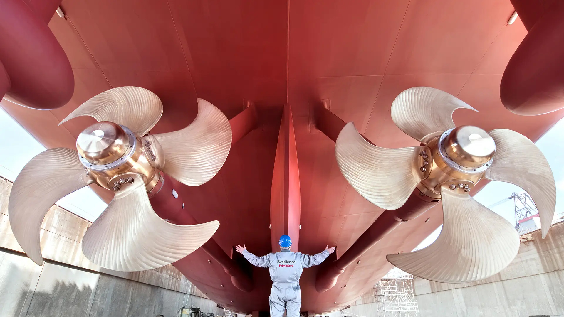 big ship in dry dock with a service employee standing below the propellers